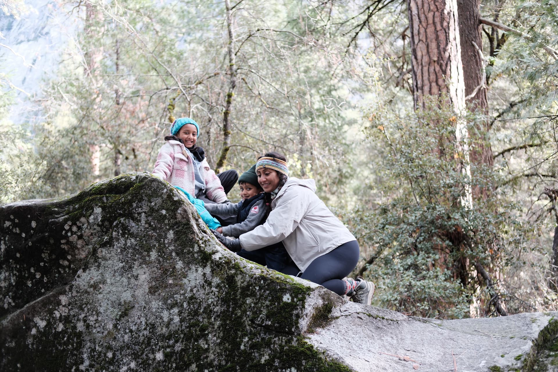 Geetha helping her children climb a mossy rock on a family hike